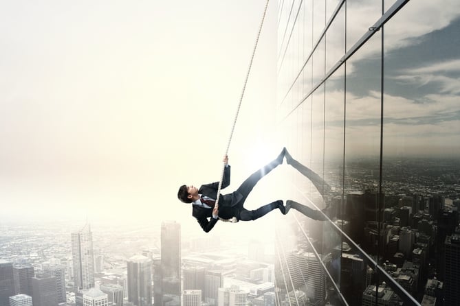 Determined businessman climbing building with help of rope.jpeg