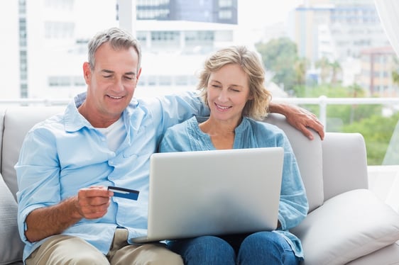 Smiling couple sitting on their couch using the laptop to buy online at home in the sitting room.jpeg